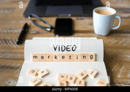 Closeup on notebook over wood table background, focus on wooden blocks with letters making Video Marketing text. Stock Photo