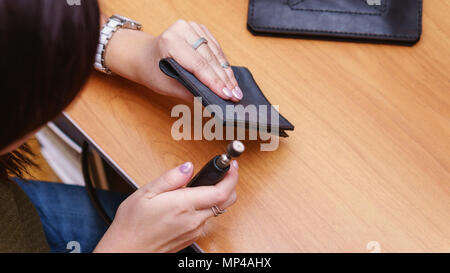 Tanner grinds edges of leather purse. Handmade. Workflow in workshop. Shooting close-up. Stock Photo