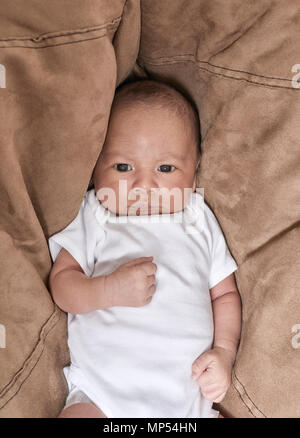 A three week old baby boy looking at the camera with his arm bent on his chest Stock Photo
