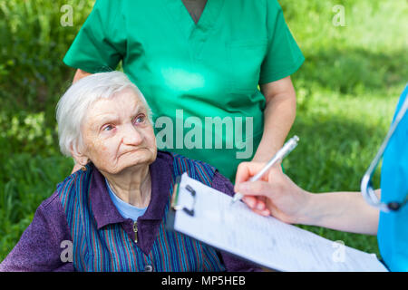 Elderly sick woman in wheelchair, medical nurses discussing treatment outdoor