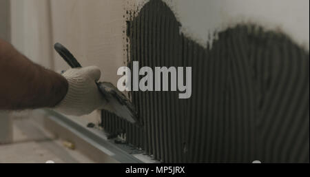 closeup worker applying concrete glue to wall before applying brick tile Stock Photo