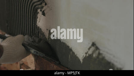 closeup worker applying concrete glue to wall before applying brick tile Stock Photo