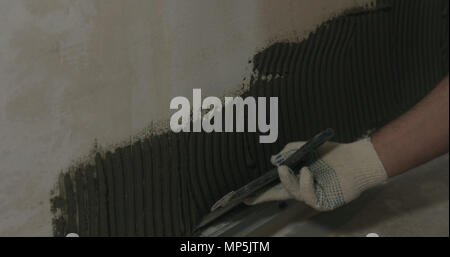 closeup worker applying concrete glue to wall before applying brick tile Stock Photo