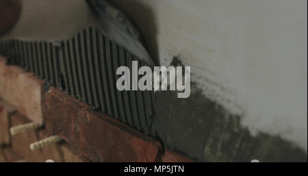 closeup worker applying concrete glue to wall before applying brick tile Stock Photo