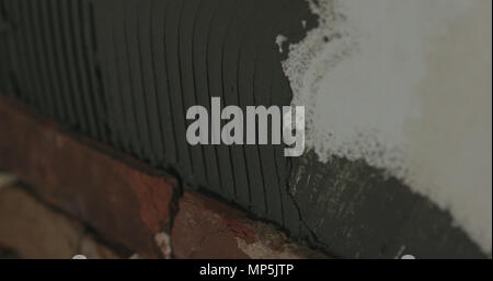 closeup worker applying concrete glue to wall before applying brick tile Stock Photo