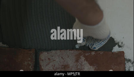 closeup worker applying concrete glue to wall before applying brick tile Stock Photo