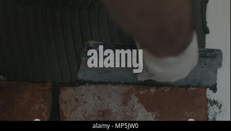 closeup worker applying concrete glue to wall before applying brick tile Stock Photo