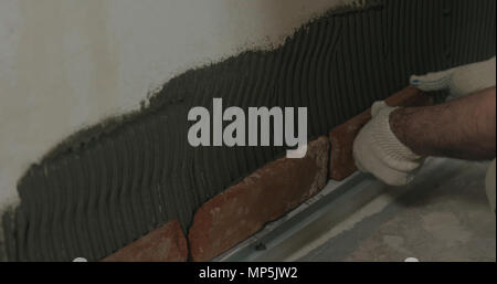 closeup worker applying brick cuts tile on the wall Stock Photo