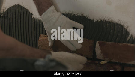 closeup worker applying brick cuts tile on the wall Stock Photo