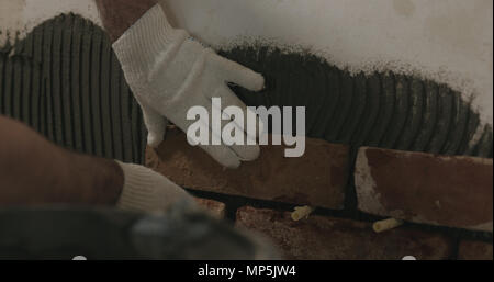 closeup worker applying brick cuts tile on the wall Stock Photo