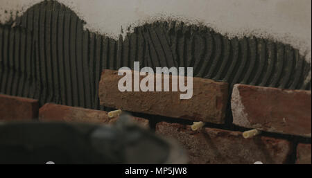 closeup worker applying brick cuts tile on the wall Stock Photo