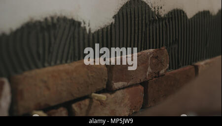 closeup worker applying brick cuts tile on the wall Stock Photo