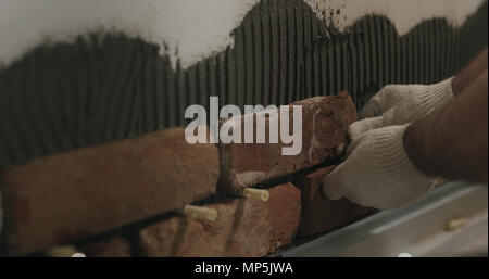 closeup worker applying brick cuts tile on the wall Stock Photo