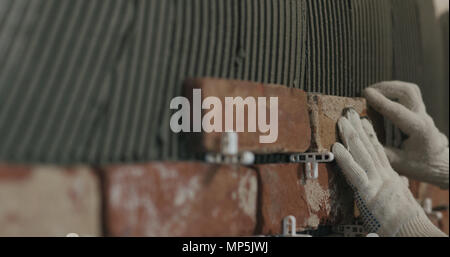 closeup worker applying brick cuts tile on the wall Stock Photo
