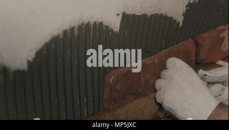 closeup worker applying brick cuts tile on the wall Stock Photo