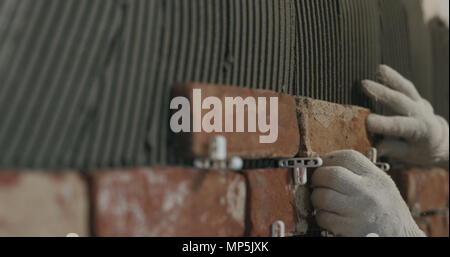 closeup worker applying brick cuts tile on the wall Stock Photo