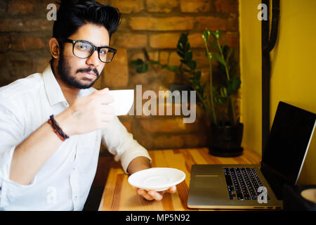 Concentrated handsome well-dressed male international student typing on laptop computer text of creative report for homework using information from we Stock Photo