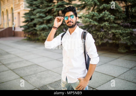 Portrait of young handsome Indian man in sunglasses and backpack an urban street Stock Photo