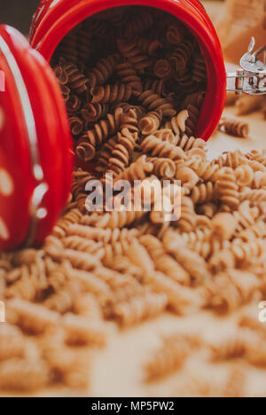 wholemeal pasta from organic spelt falling out of a red jar on a paper craft Stock Photo