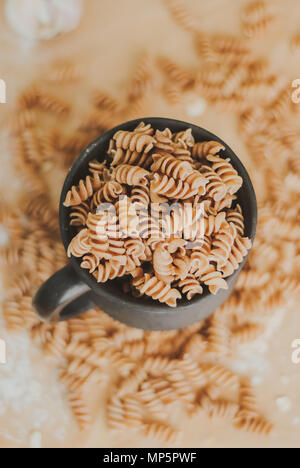 wholemeal pasta from organic spelt falling out of a black mug on a paper craft Stock Photo