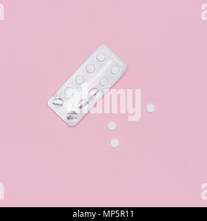 White pills and blister pack on pink pastel colored background. Pharmaceutical industry minimal still life flat lay background. Opioid epidemic.
