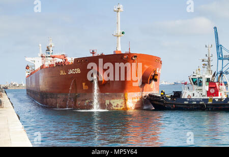 Oil tanker pumping ballast water as tug boat guides ship onto berth in port Stock Photo