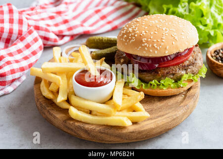 Homemade beef burger and french fries with ketchup on wooden board on gray concrete background. Horizontal composition. Tasty burger and fries. Fast f Stock Photo