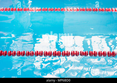 Blue pool water and red swimming lane marker in swimming pool with sun reflections. Abstract blurred pattern. Stock Photo