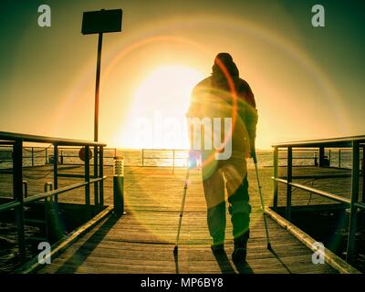 Gloomy nostalgic silhouette of sad lonely melancholic adult man with hooded jacket standing on lake bridge within  early morning and thinking Stock Photo