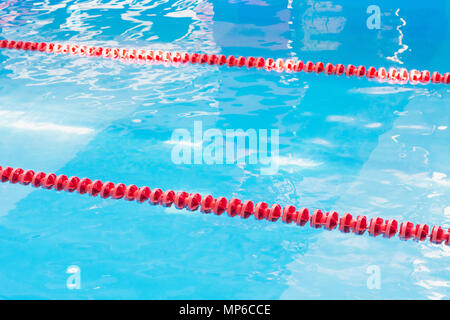 Blue pool water and red swimming lane marker in swimming pool with sun reflections. Abstract blurred pattern. Stock Photo