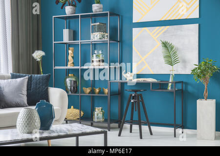 Black stool at desk with leaf against blue wall with posters in workspace interior with shelves Stock Photo