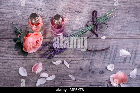 Spa set with rose petals oil , Perfumed Rose Water in glass bottles and lavender with purple ribbon on wooden background, rustic style. Massage, aromatherapy and organic cosmetics concept. Stock Photo