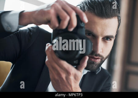 Young bearded stylish businessman leader indoors at office candid holding professional camera taking photo concentrated on shot close-up Stock Photo