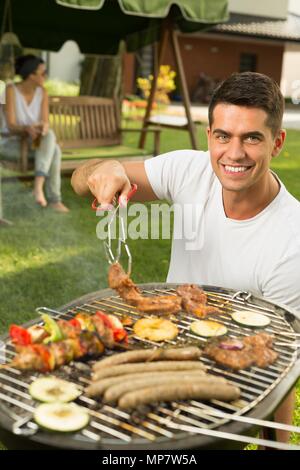 Shot of a happy young man tending a barbecue Stock Photo