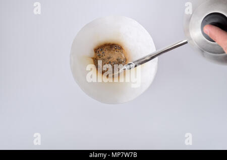 The stream of hot water from the kettle is poured on the filter  in the vintage coffee maker isolated on the blank background. Top of view. Stock Photo