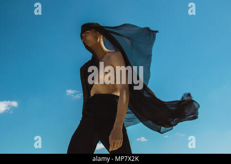 Guy with black scarf and wind on sky background in dessert Stock Photo