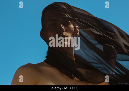 Guy with black scarf and wind on sky background in dessert Stock Photo