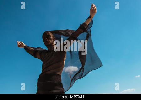 Guy with black scarf and wind on sky background in dessert Stock Photo