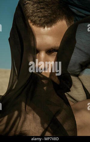 Guy with black scarf and wind on sky background in dessert Stock Photo