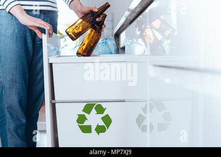 Aware person sorting waste in modern kitchen with special bin with green symbol for glass bottles Stock Photo