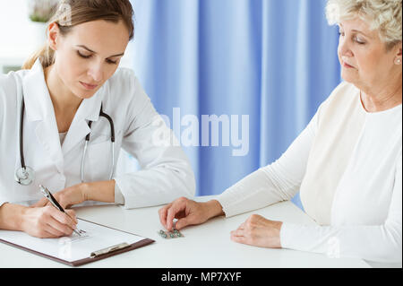 Professional doctor with stethoscope writing prescription for dietary supplements to a patient Stock Photo
