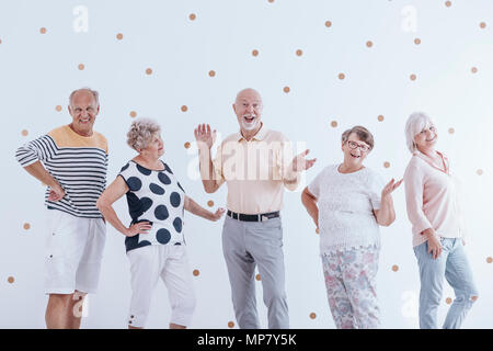 Senior man and his friends celebrating his birthday against wallpaper with gold dots
