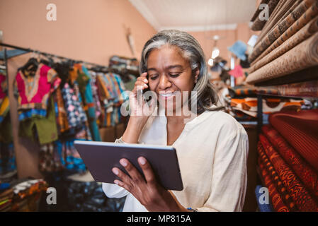 Smiling fabric shop owner using a tablet and cellphone Stock Photo