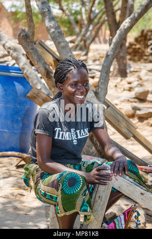 Smiling local African woman with braided hair sitting working outdoors at Katundu creative trade workshop, Likoma Island, Lake Malawi, Malawi, Africa Stock Photo