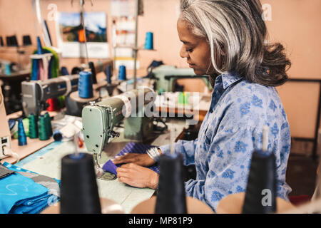 Mature woman sewing cloth in her clothes workshop Stock Photo