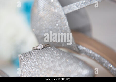 Engagement ring sitting on a sparkly pair of bridal shiny shoes on her wedding day, silver shoes and diamond ring Stock Photo