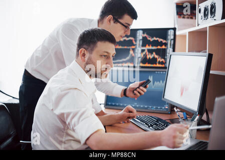 Businessmen trading stocks online. Stock brokers looking at graphs, indexes and numbers on multiple computer screens. Colleagues in discussion in traders office. Business success concept Stock Photo