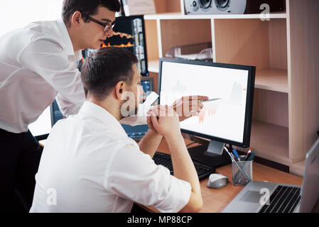 Businessmen trading stocks online. Stock brokers looking at graphs, indexes and numbers on multiple computer screens. Colleagues in discussion in traders office. Business success concept Stock Photo
