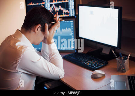 Stressful day at the office. Young businessman holding hands on his face while sitting at the desk in creative office. Stock Exchange Trading Forex Finance Graphic Concept Stock Photo
