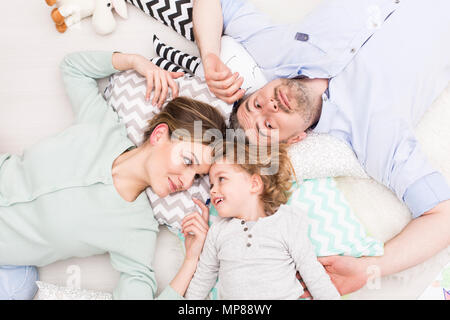 Shot from above of a smiling young family lying on the floor and relaxing among cushions